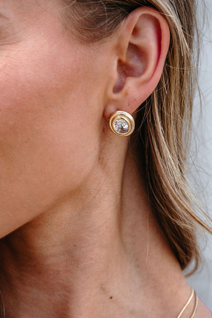 Close-up of a person wearing Gold Dipped Oval Stud Earrings, each with an elegant crystal center.