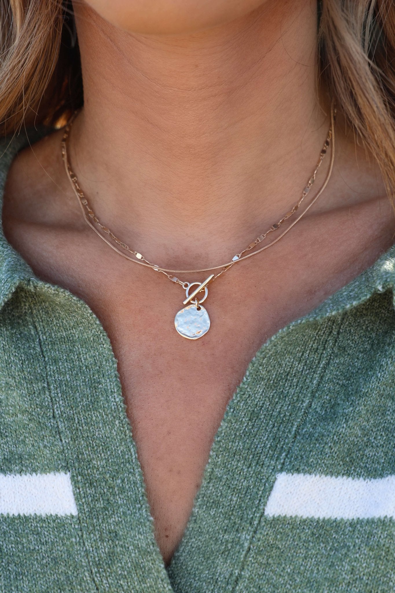 Close-up of a person wearing the Gold Double Layer Hammered Pendant Necklace over a green sweater with white stripes.