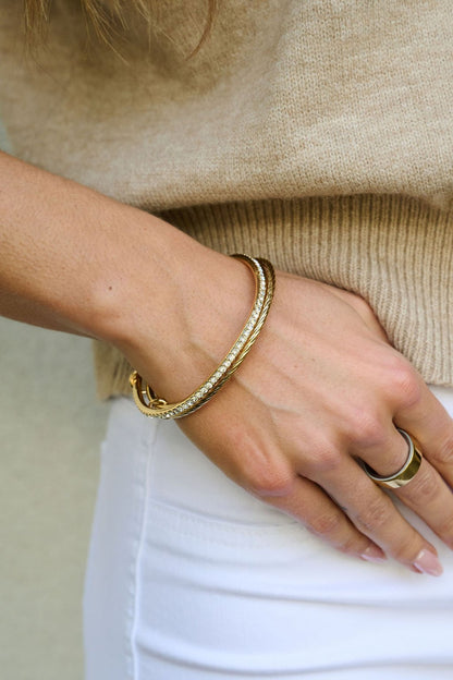 Wearing the Gold Double Layered Bracelet Set, a person in a beige sweater and white pants rests their hand on their hip.
