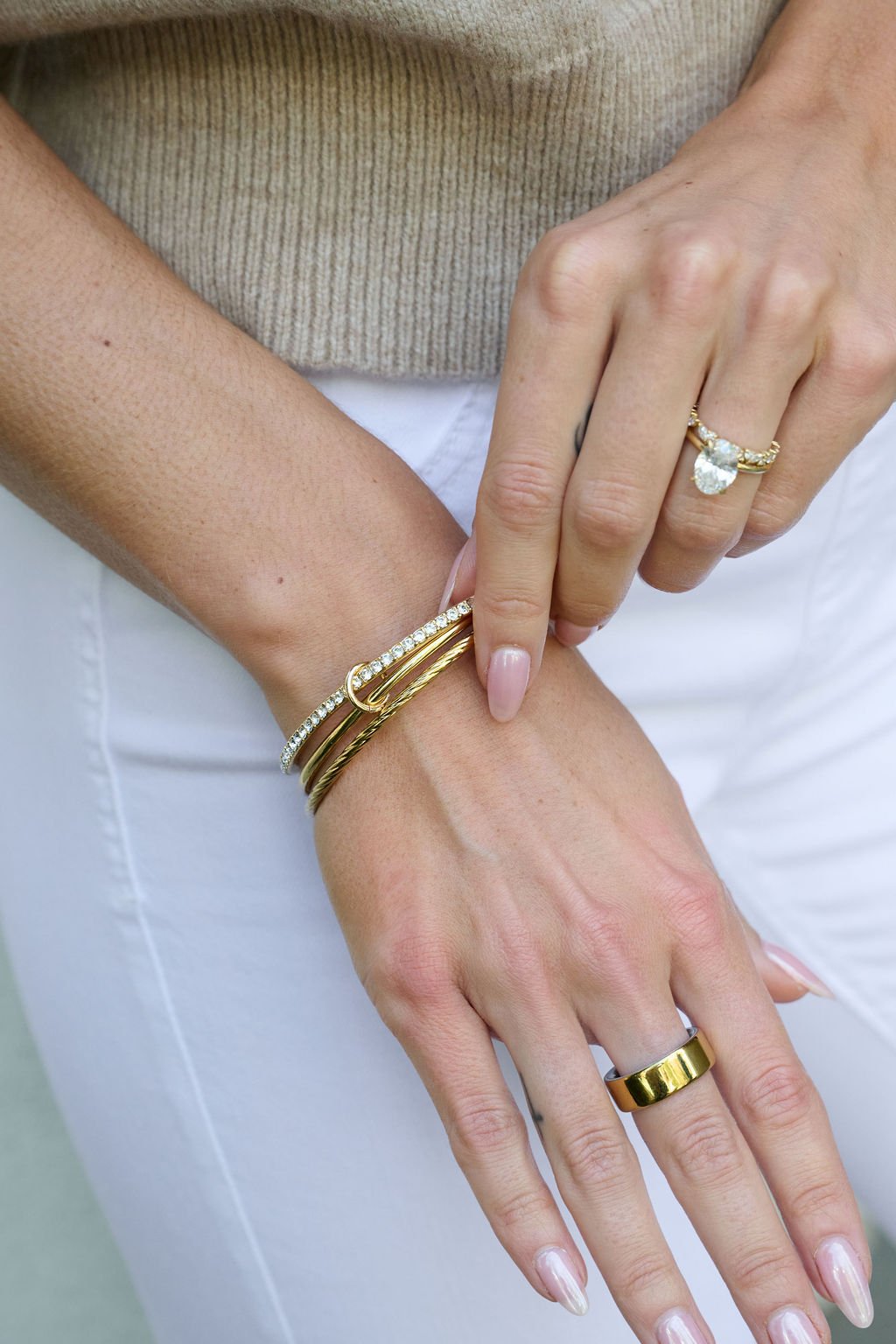 A woman in white pants and a beige top with manicured nails wears the Gold Double Layered Bracelet Set and matching rings.