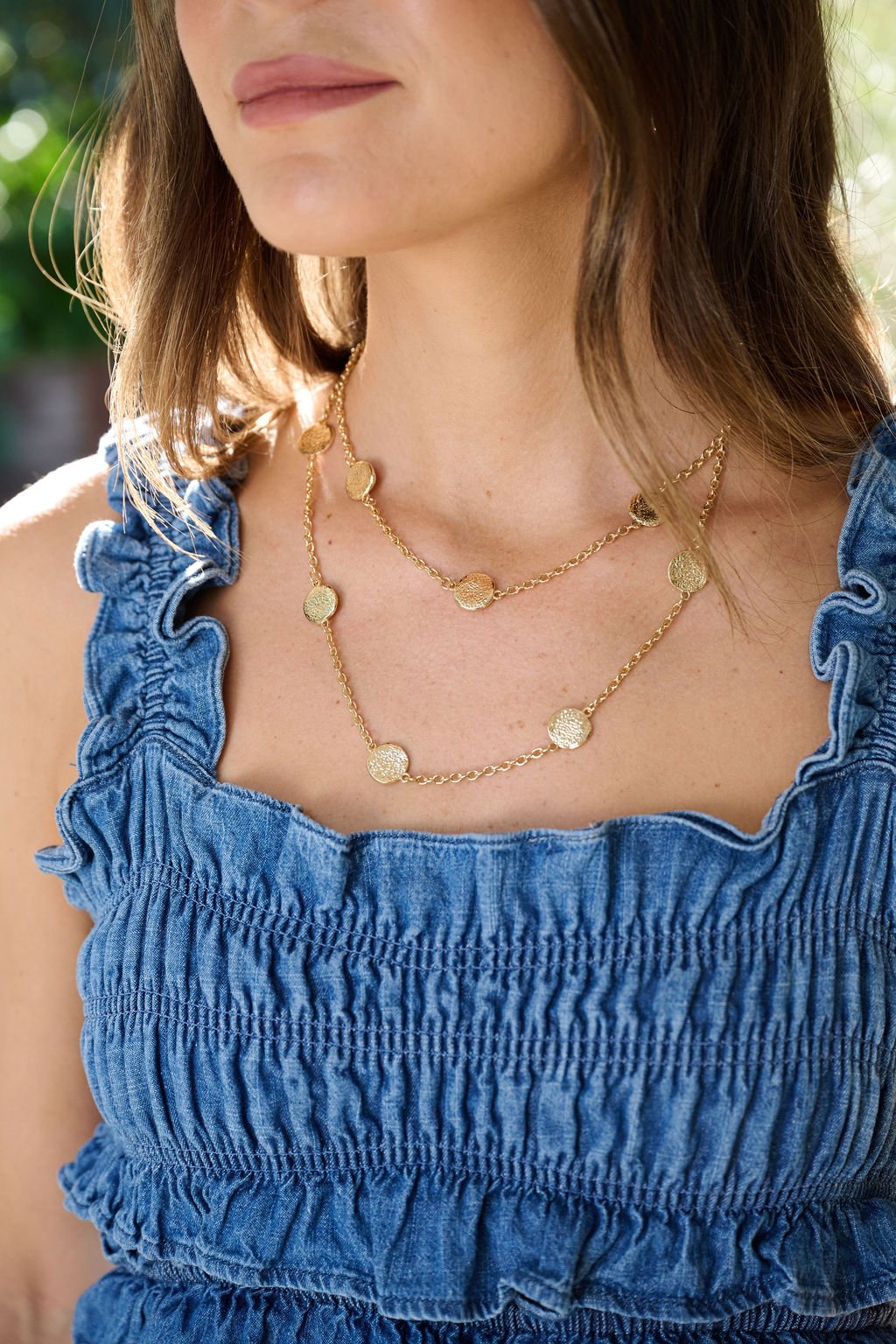 Woman wearing a blue ruffled denim dress and a Gold Double Layered Chain Coin Necklace, shown from shoulders to lips.