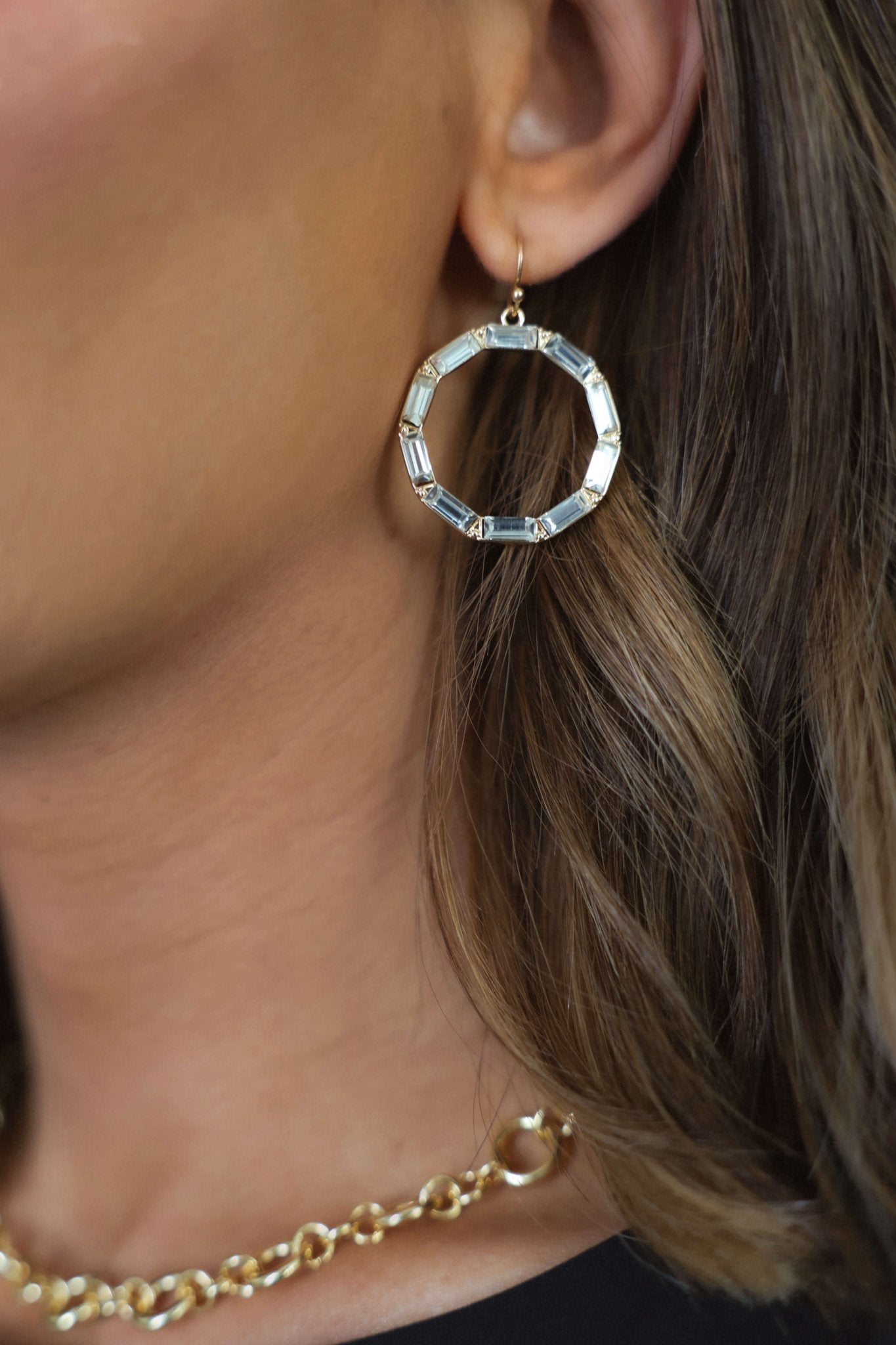 Close-up of a woman's ear wearing Gold Gem Dangle Hoop Earrings, with part of a gold chain necklace visible.