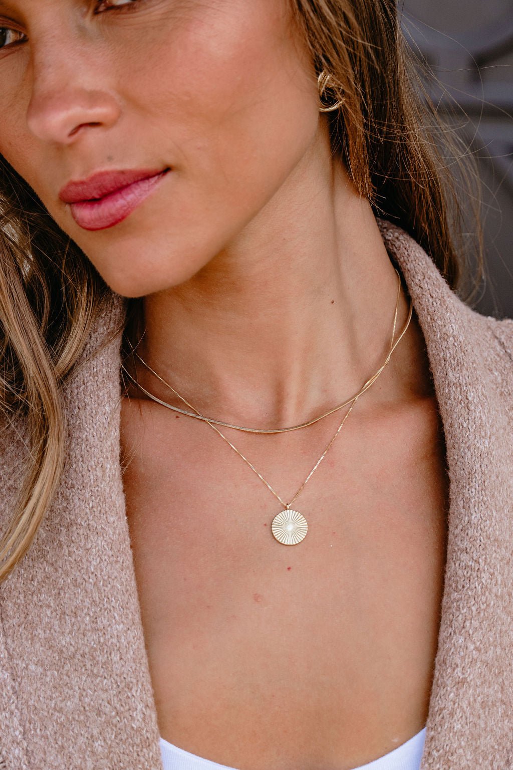 Woman wears a Gold Layered Disc Pendant Necklace and beige sweater; close-up highlights her neck and jewelry.