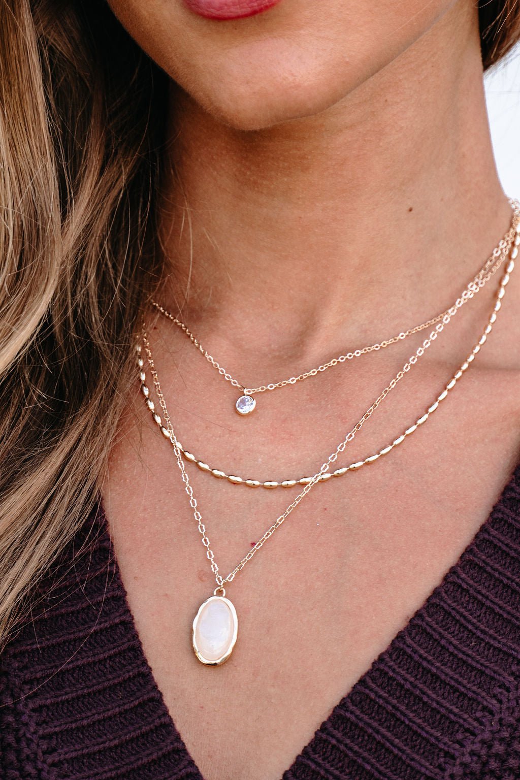 A woman wears the Gold Layered Natural Stone Necklace over her purple knit top, layering the elegant chains.