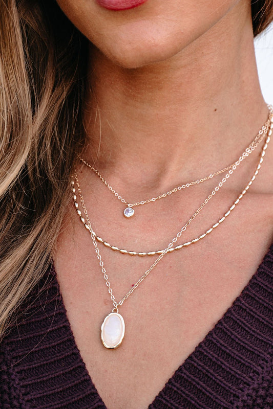 A woman wears the Gold Layered Natural Stone Necklace over her purple knit top, layering the elegant chains.