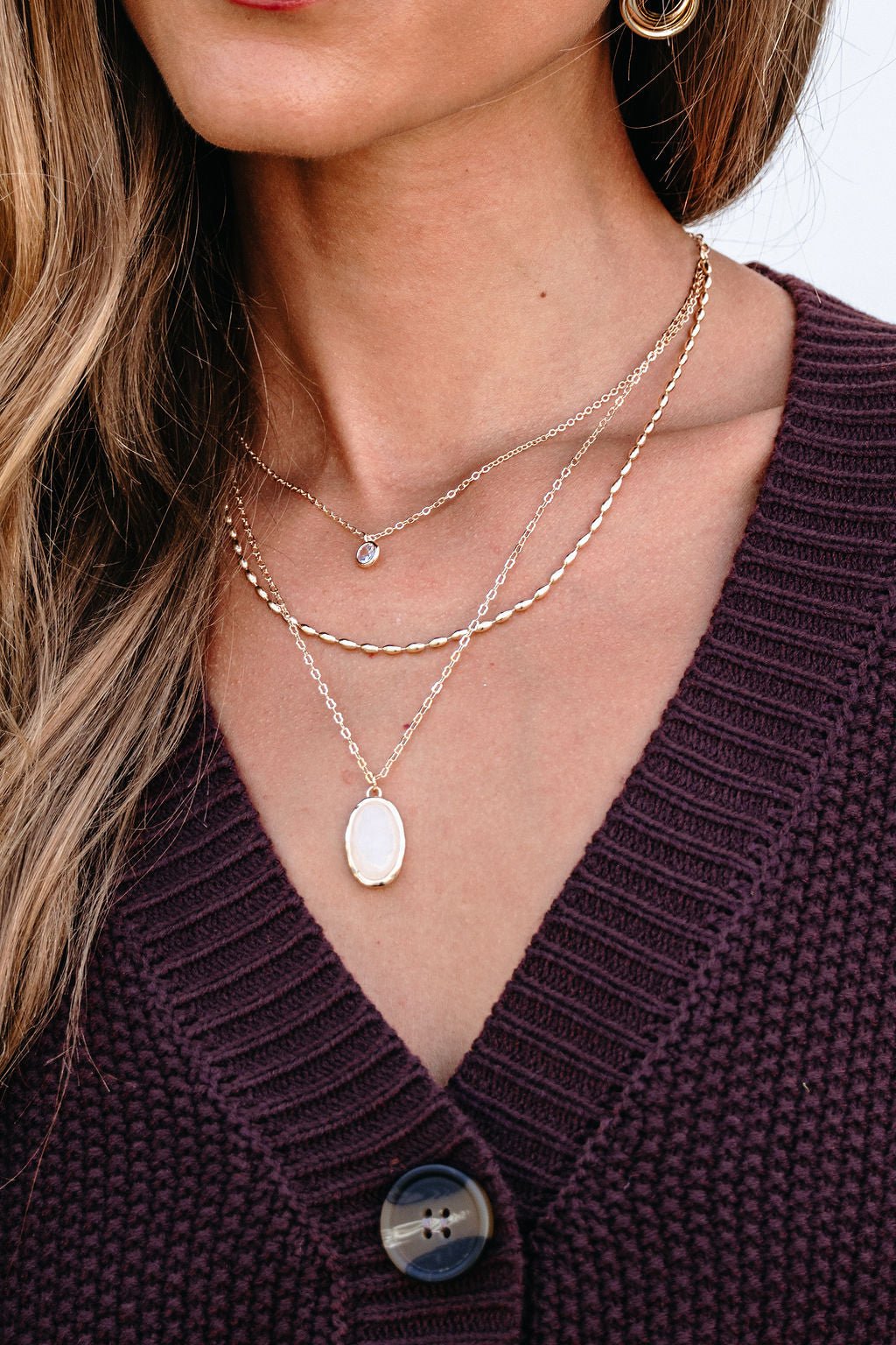 A woman wears a Gold Layered Natural Stone Necklace and a purple knit cardigan with large buttons.