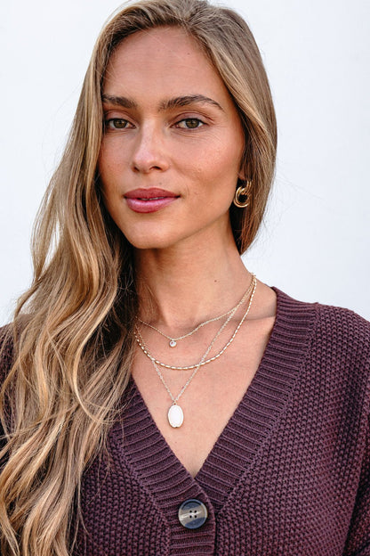 Woman with long blonde hair wears the Gold Layered Natural Stone Necklace, hoop earrings, and a purple knit sweater against a white background.