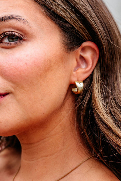 Close-up of a woman wearing Gold Matte Small Hoop Earrings, showing part of her face, hair, and ear.
