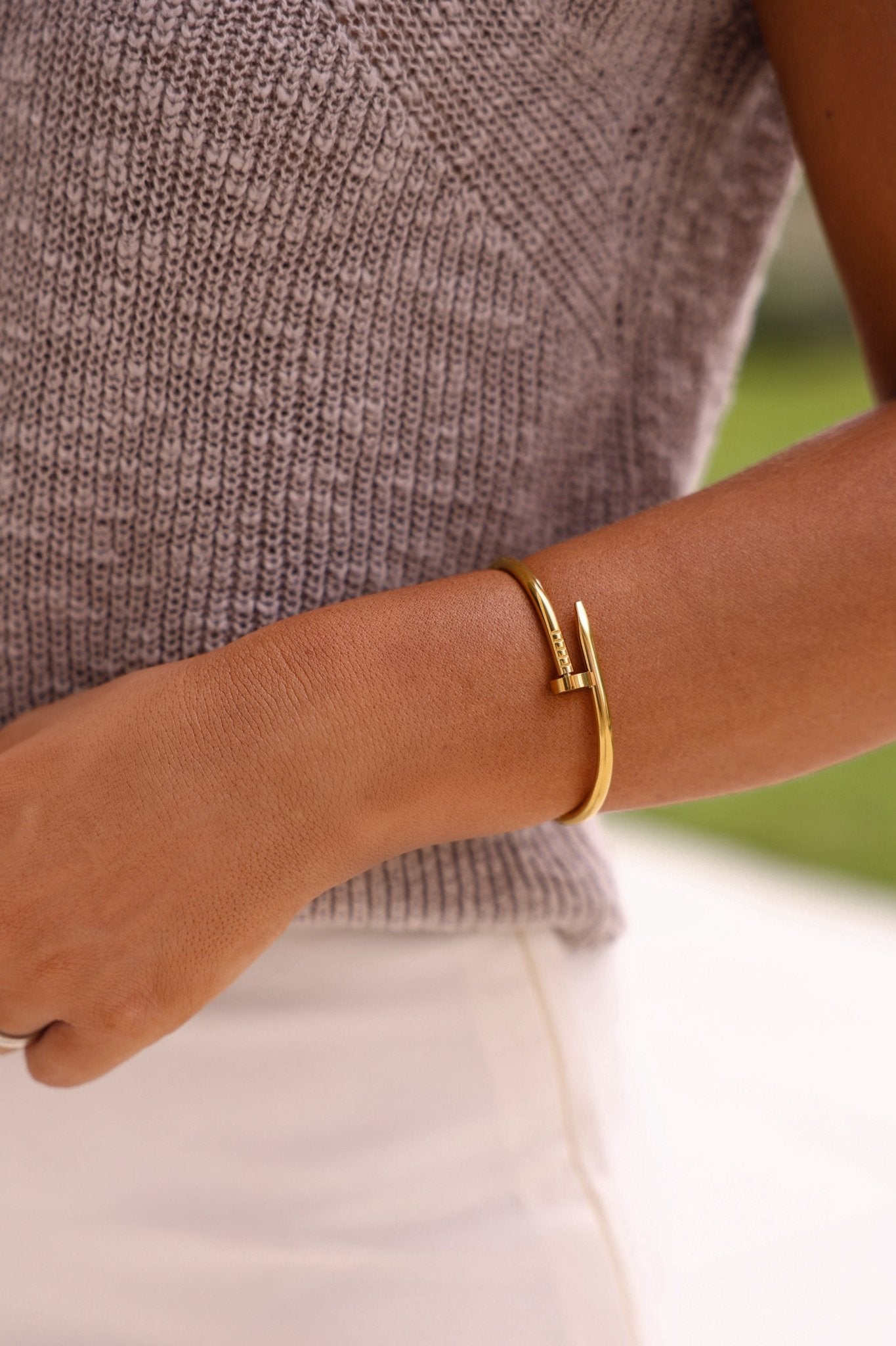Someone wearing the Gold Open Bangle Bracelet, a grey knit top, and white pants in a blurred outdoor setting.