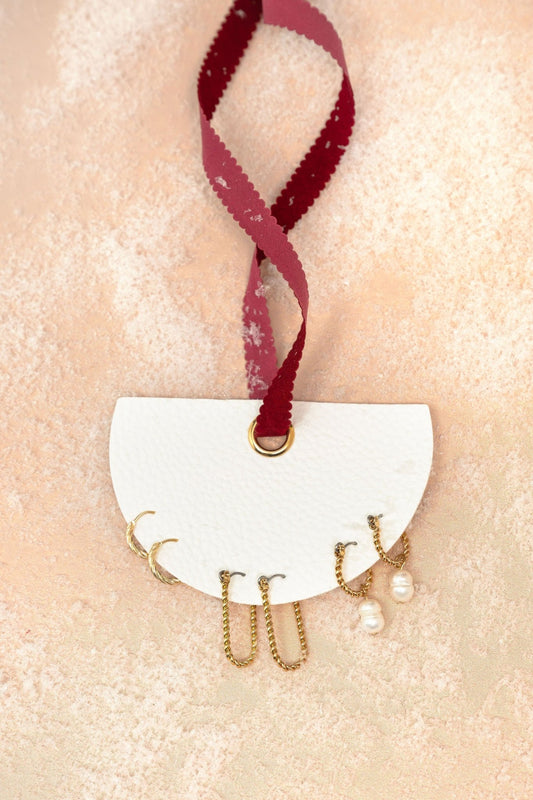 Gold Pearl Charm Twisted Hoop Earrings Set displayed on a white semi-circle holder with a red ribbon on beige textured surface.