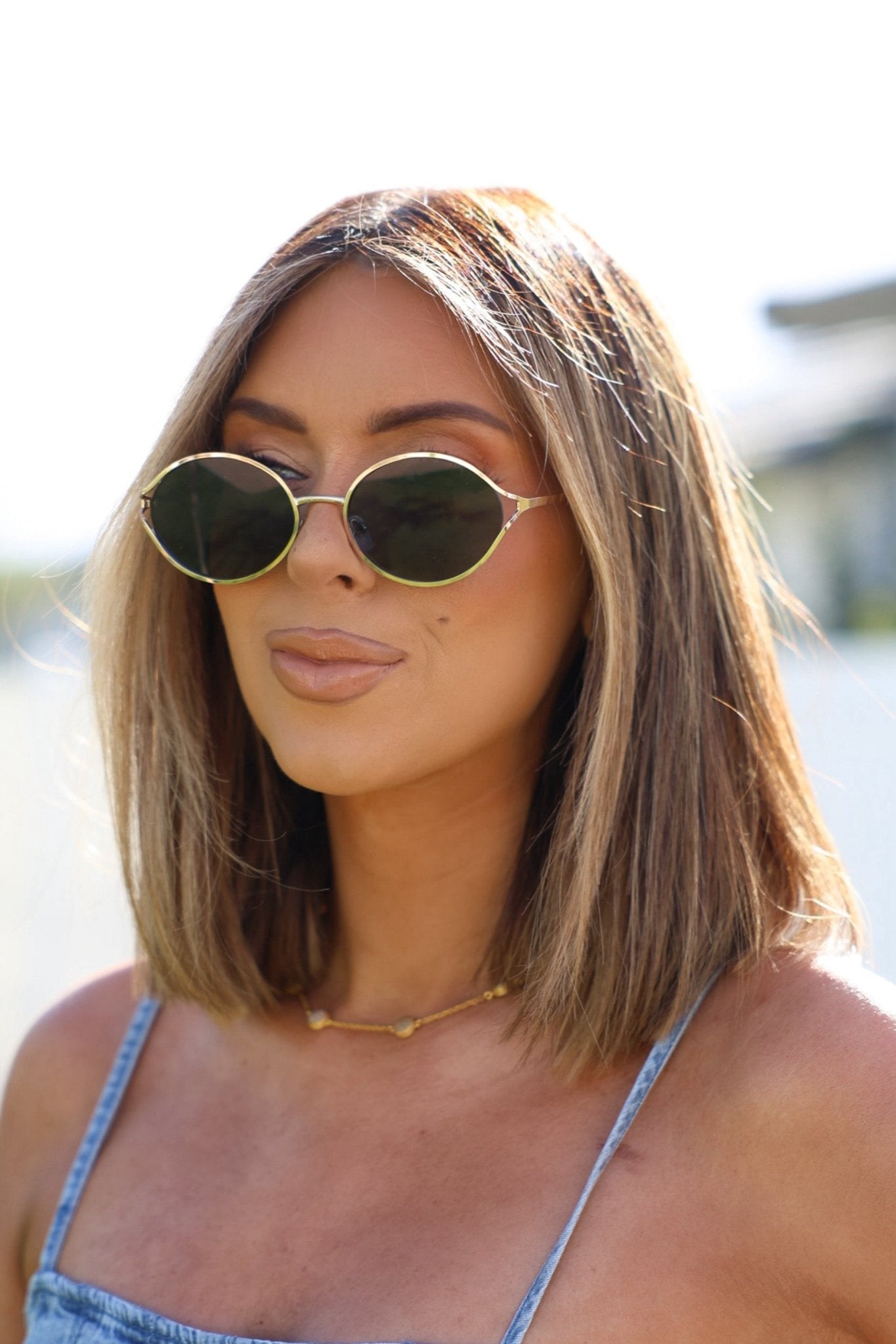 Woman with straight, shoulder-length blonde hair wears Gold Smoke Lens Round Sunglasses, gold necklace, and sleeveless top outside.