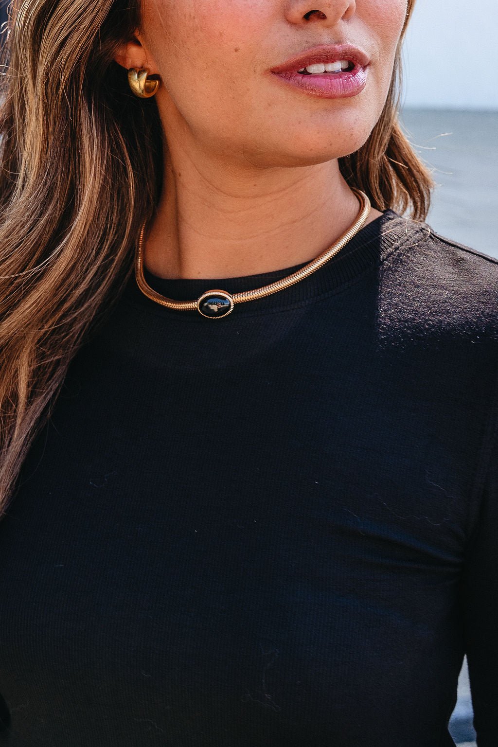 Woman wearing a black top, gold hoop earrings, and a Gold Snake Chain Black Oval Pendant Necklace, standing outdoors.
