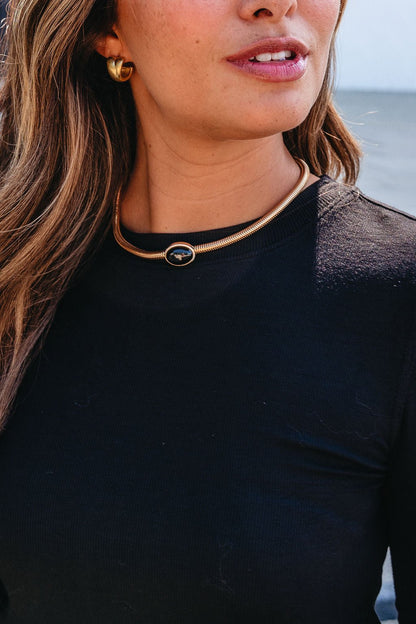 Woman wearing a black top, gold hoop earrings, and a Gold Snake Chain Black Oval Pendant Necklace, standing outdoors.