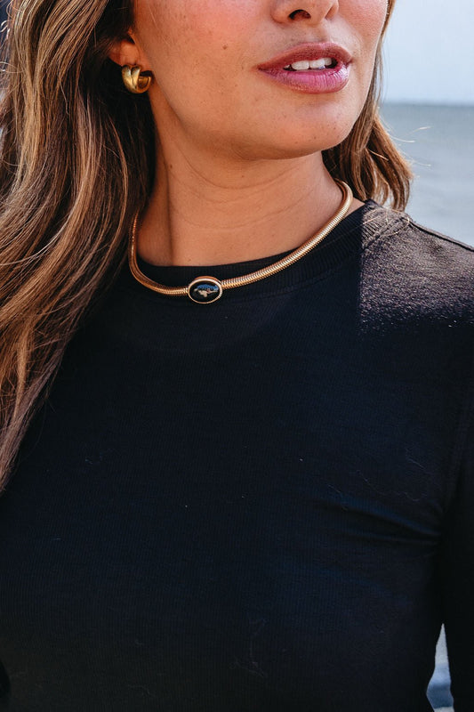 Woman wearing a black top, gold hoop earrings, and a Gold Snake Chain Black Oval Pendant Necklace, standing outdoors.