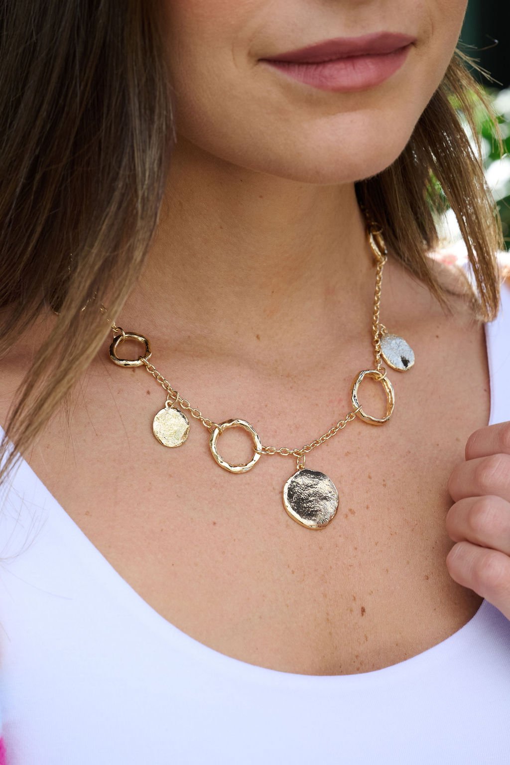 A woman wears the Gold Warped Hoop & Coin Pendant Necklace as an effortless everyday accessory over a white top.