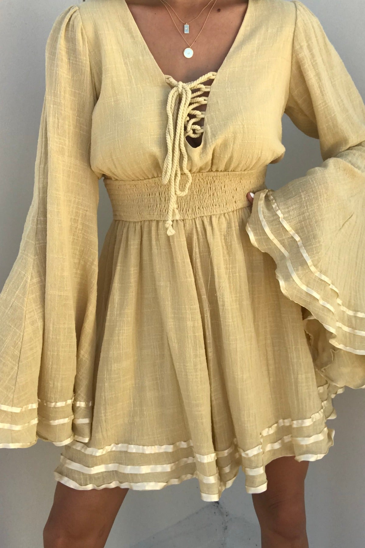 A woman models the Golden Hour Bell Sleeve Romper with lace-up front and ruffled hem against a plain backdrop.