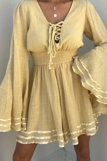 A woman models the Golden Hour Bell Sleeve Romper with lace-up front and ruffled hem against a plain backdrop.