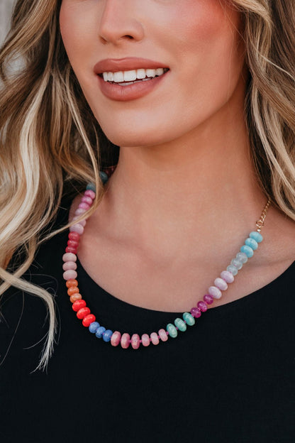 Woman wearing a black top and the Golden Sol Beaded Necklace, smiling with wavy blonde hair partially visible.