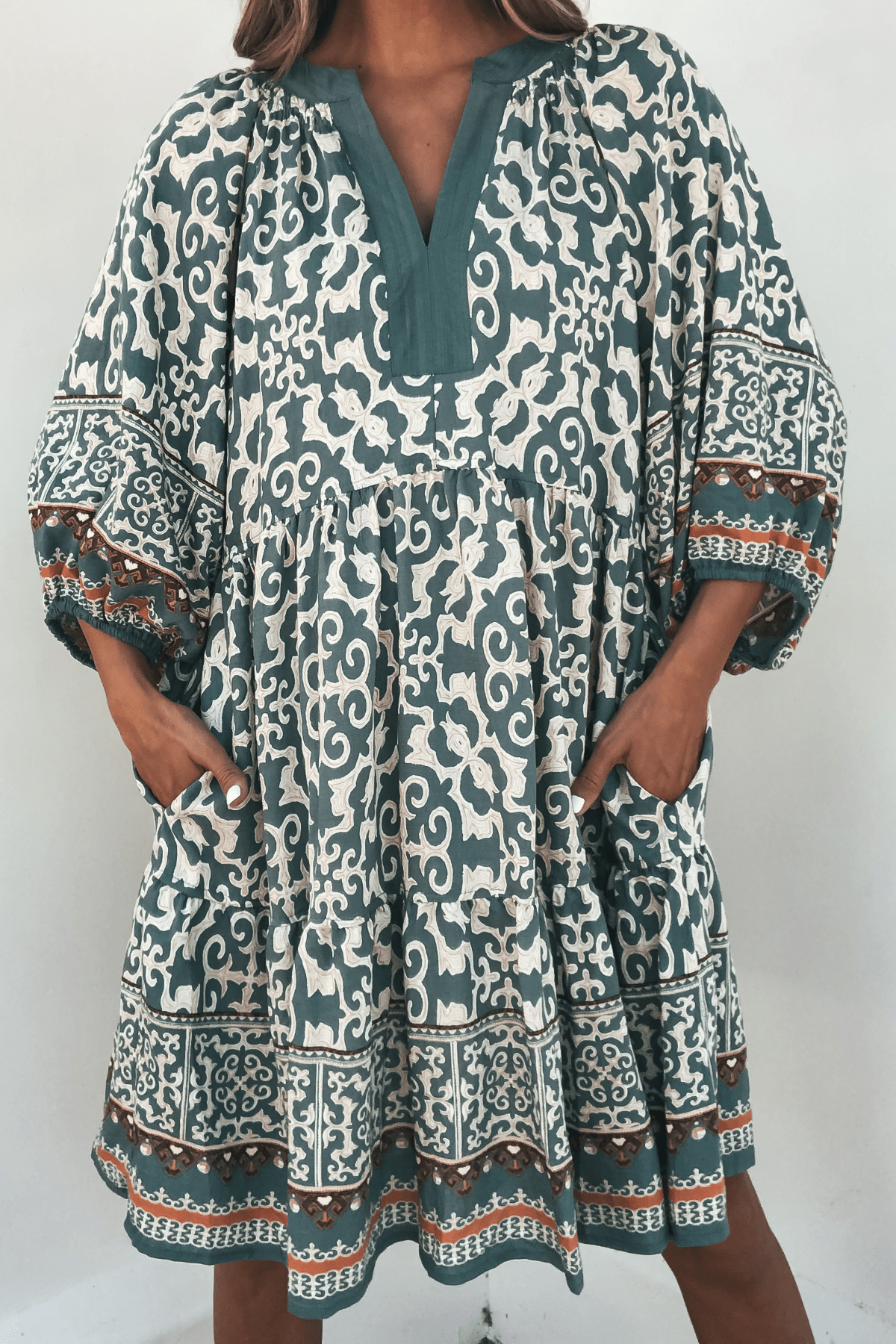 Someone wears the Green Border Print Tiered Mini Dress - FINAL SALE, featuring a loose fit, tiered design, and pockets.