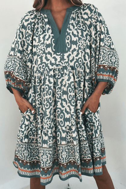 Someone wears the Green Border Print Tiered Mini Dress - FINAL SALE, featuring a loose fit, tiered design, and pockets.