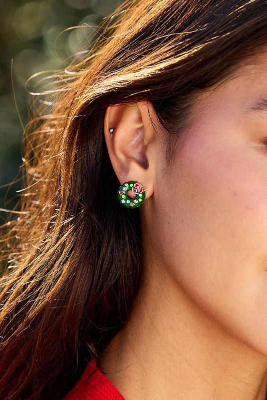 A woman with long brown hair wears Green Holiday Wreath Stud Earrings adorned with green, red, and white beads for a festive look.
