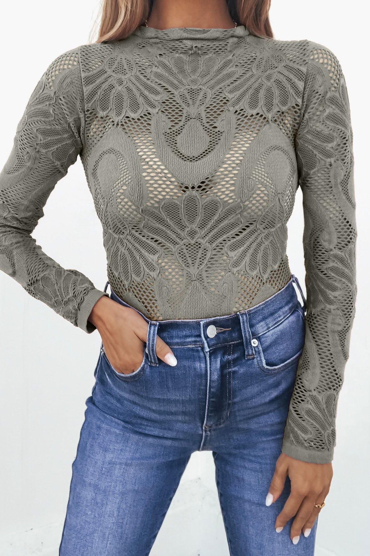 Woman wears a Green Mock Neck Fishnet Top with long sleeves and blue high-waisted jeans.