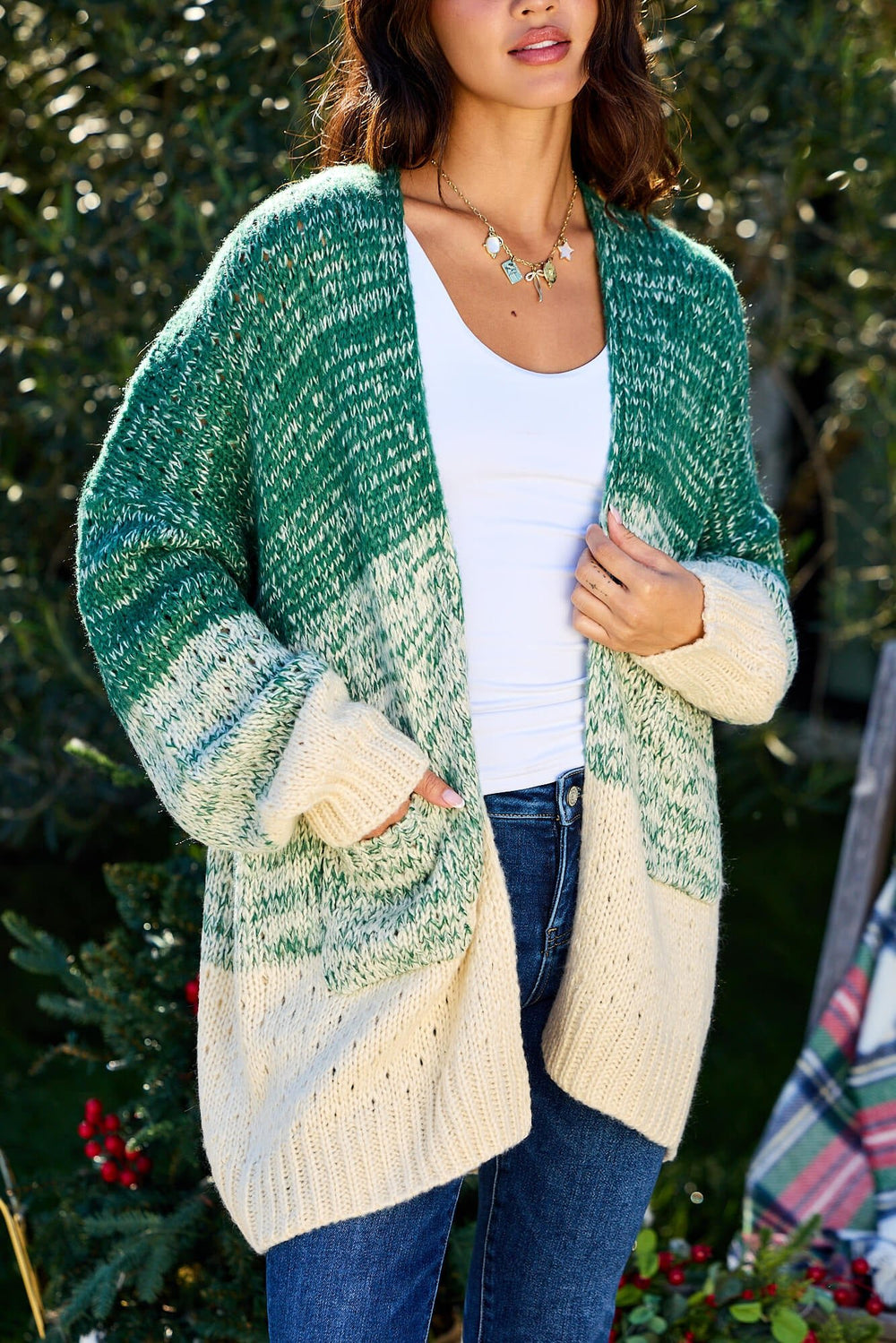 Woman wears the Green Ombre Open Front Cardigan - FINAL SALE over a white top and jeans, standing outdoors with greenery behind her.