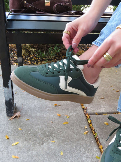 Someone ties the laces of Green Remus Lace Up Sneakers - DOORBUSTER while sitting on an outdoor bench.