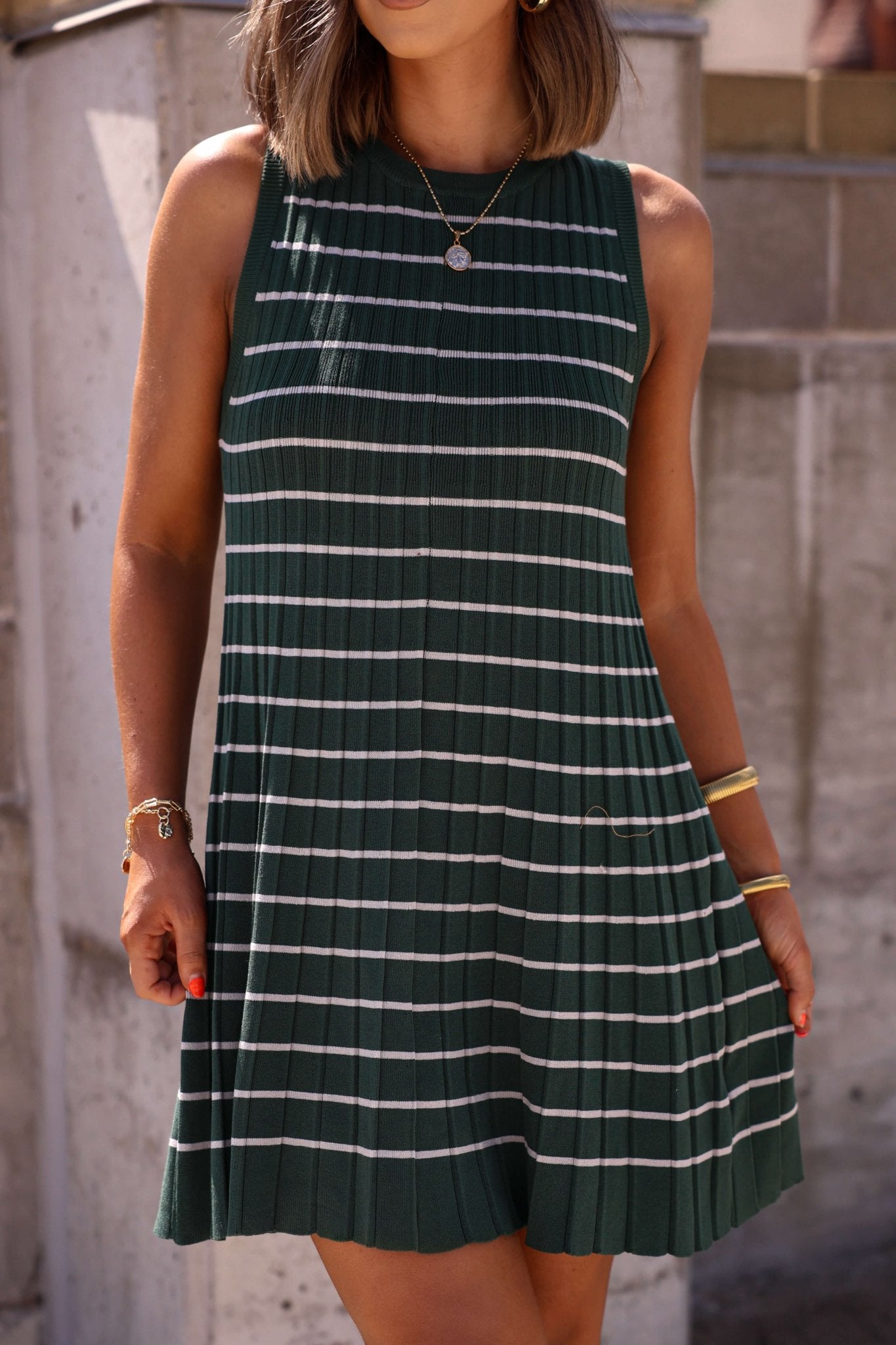 Woman in a Green Stripe Pleated Mini Dress - FINAL SALE, with gold jewelry and red nails, outdoors. A Magnolia Exclusive look.