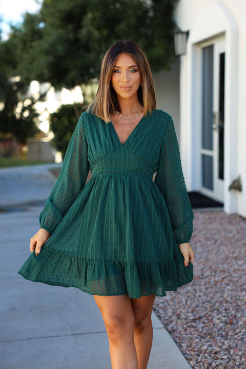 A woman models the Green Swiss Dot Ruffled Mini Dress outdoors, smiling and holding out the skirt for the camera.