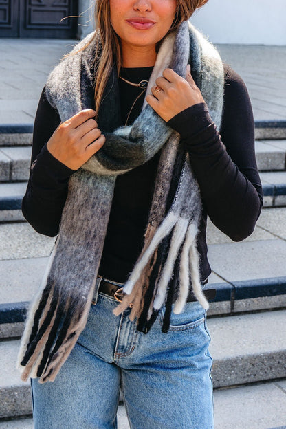 Woman wearing a Grey and Mint Gingham Fringe Scarf, black long-sleeve top, and light blue jeans—an essential cozy accessory.