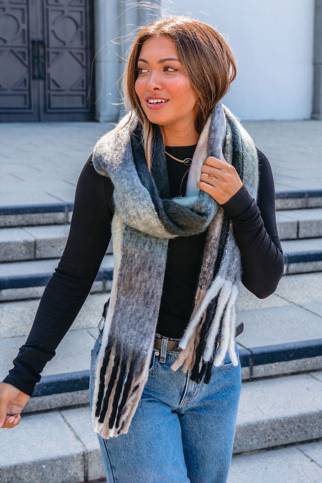A woman stands outside in a cold-weather outfit, wrapped warmly in a Grey and Mint Gingham Fringe Scarf.