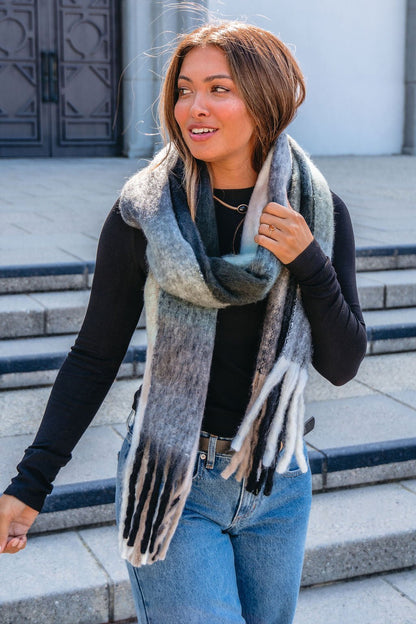 A woman stands outside in a cold-weather outfit, wrapped warmly in a Grey and Mint Gingham Fringe Scarf.