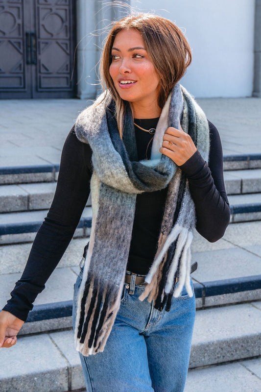 A woman stands outside in a cold-weather outfit, wrapped warmly in a Grey and Mint Gingham Fringe Scarf.