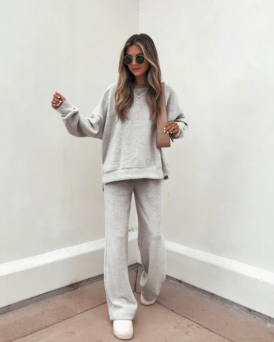 Woman in a Grey Brushed Lounge Sweatshirt—FINAL SALE—stands against a white wall with a bag and sunglasses.