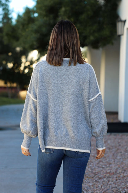 A woman in a Grey Contrast Detail Pullover Sweater and blue jeans stands outdoors, perfect for a fall wardrobe.