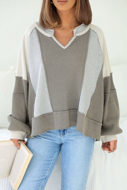 Woman in a Grey Contrast Frayed Edge Pullover and blue jeans holds an open book, standing indoors against a white background.