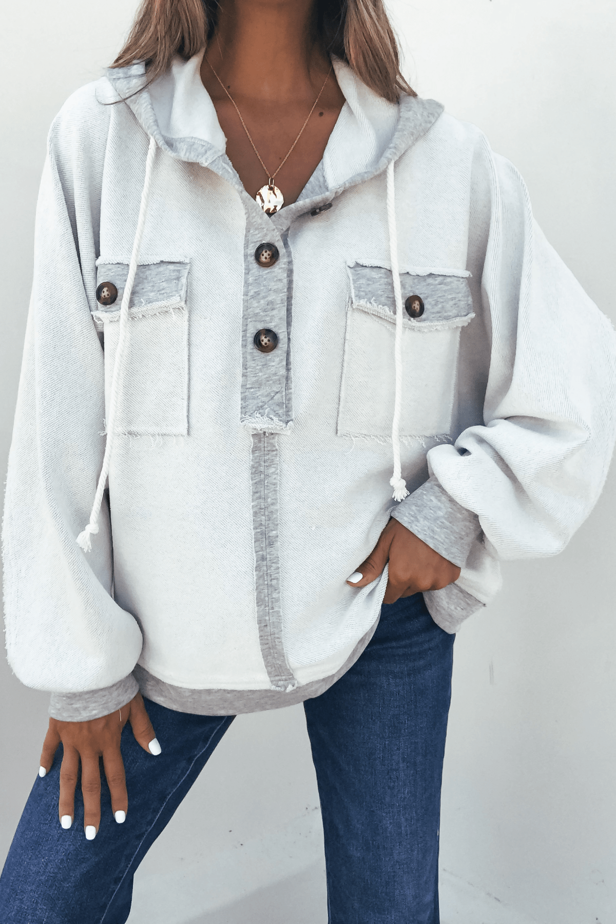 Woman wearing the Grey Contrast Half Button Up Hooded Sweatshirt with front pockets, blue jeans, and layered necklaces.