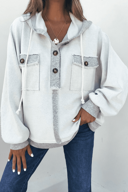 Woman wearing the Grey Contrast Half Button Up Hooded Sweatshirt with front pockets, blue jeans, and layered necklaces.