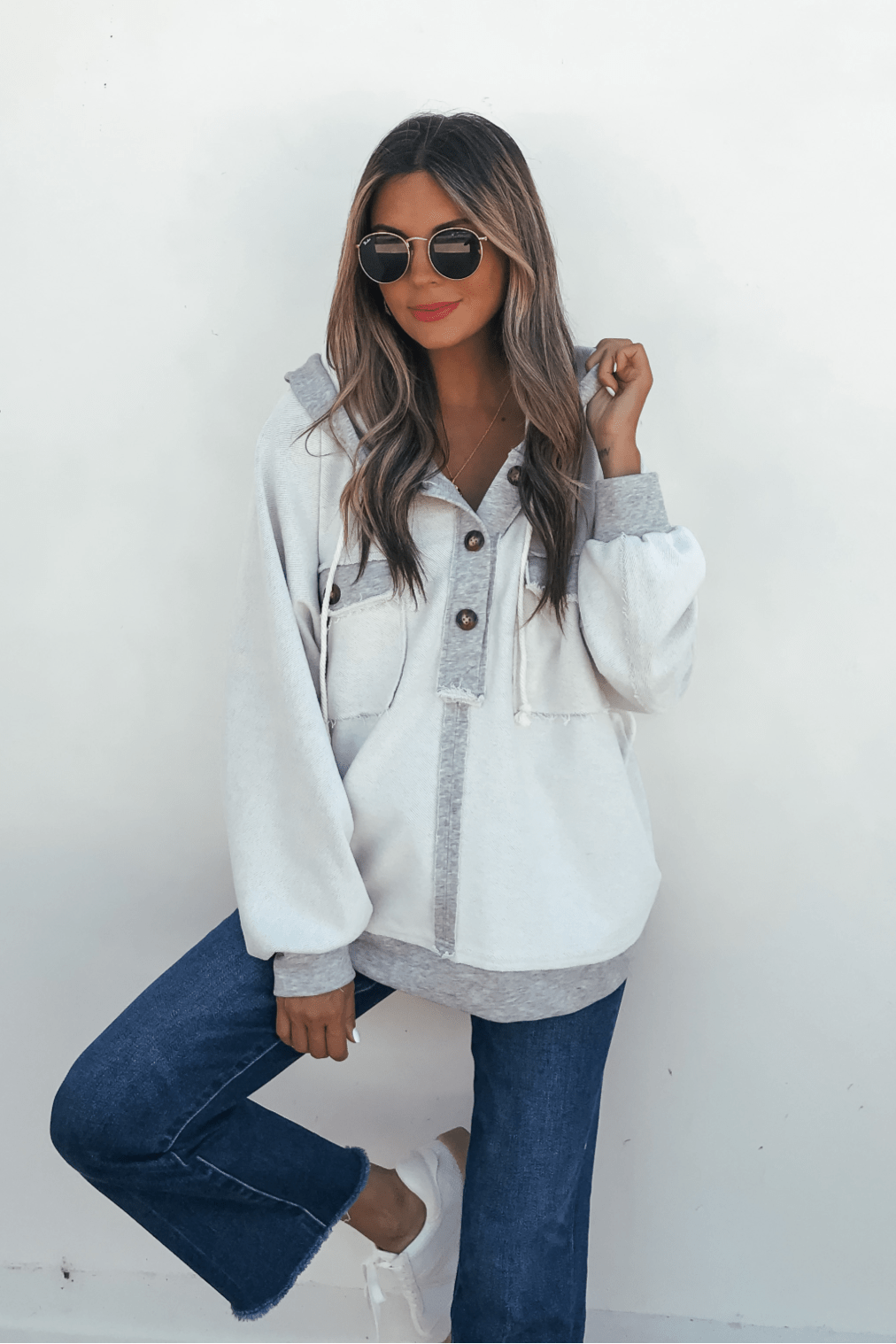 Woman in sunglasses and blue jeans poses in a Grey Contrast Half Button Up Hooded Sweatshirt against a white wall.