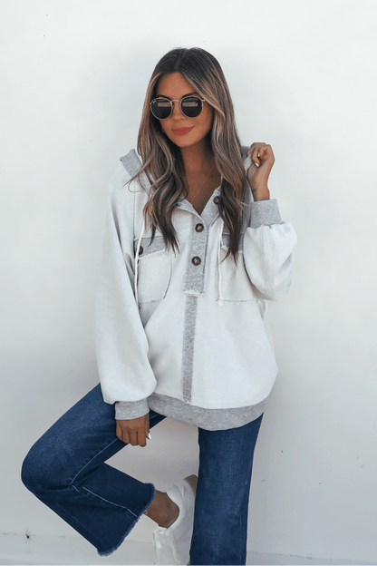 Woman in sunglasses and blue jeans poses in a Grey Contrast Half Button Up Hooded Sweatshirt against a white wall.