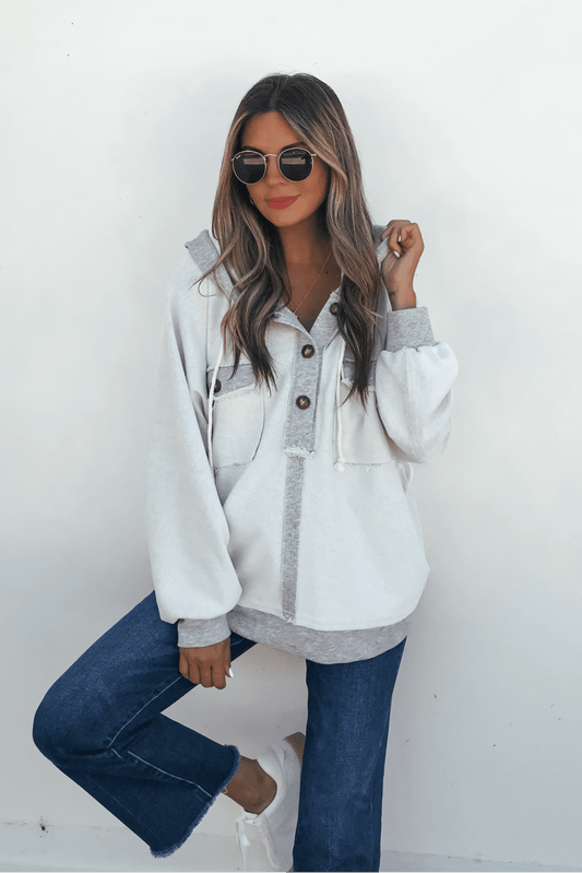Woman in sunglasses and blue jeans poses in a Grey Contrast Half Button Up Hooded Sweatshirt against a white wall.