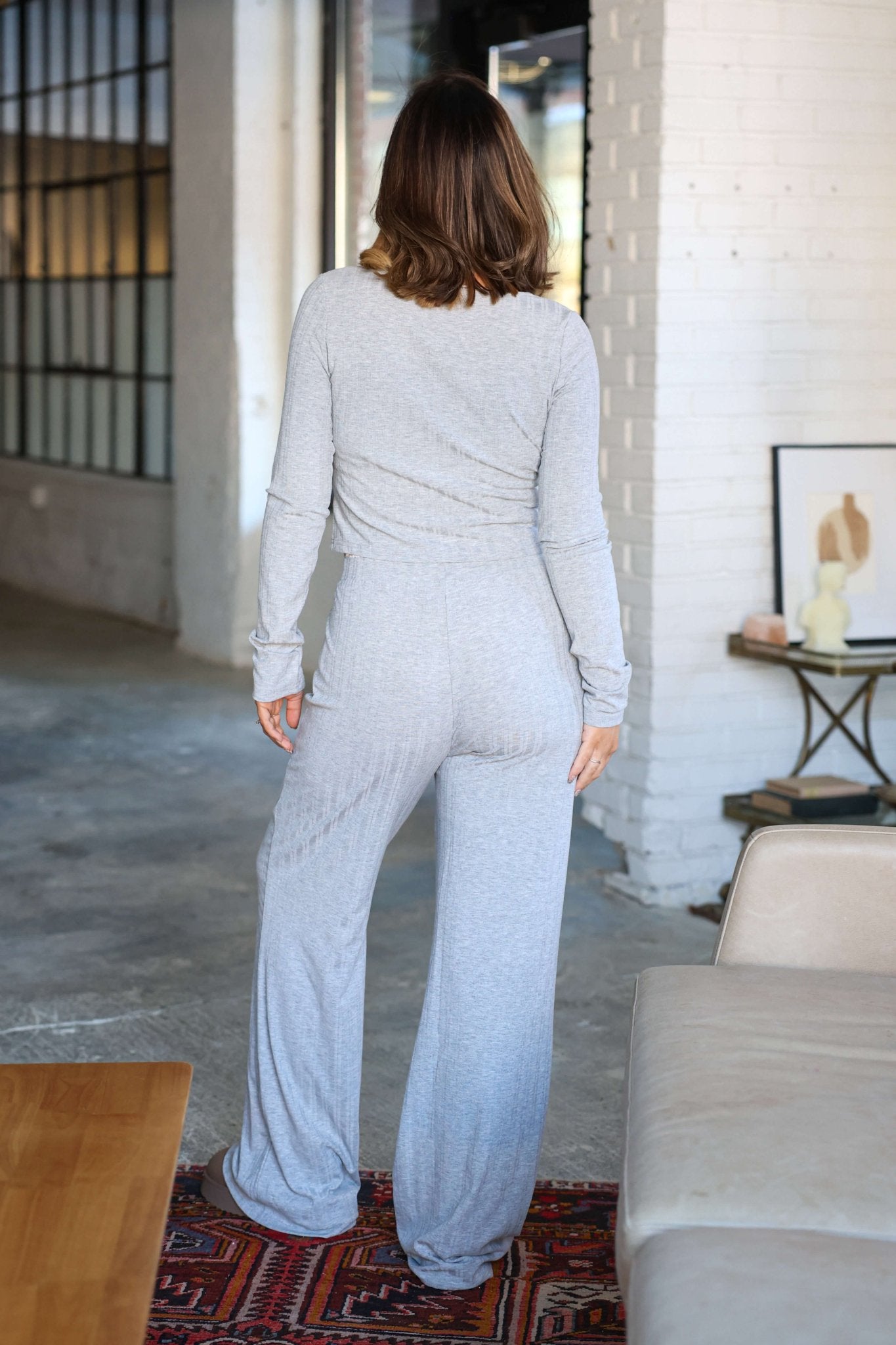 A woman in a Grey Lace Trim Lounge Set stands indoors with her back to the camera, redefining luxury loungewear.