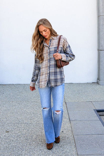 Woman with long hair wears a Grey Plaid Button Down Top, ripped jeans, brown shoes, and a brown shoulder bag while walking outside.
