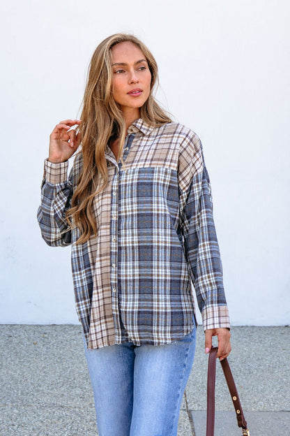 Woman wears a Grey Plaid Button Down Top and light blue jeans outside, holding a brown strap with a white wall behind her.