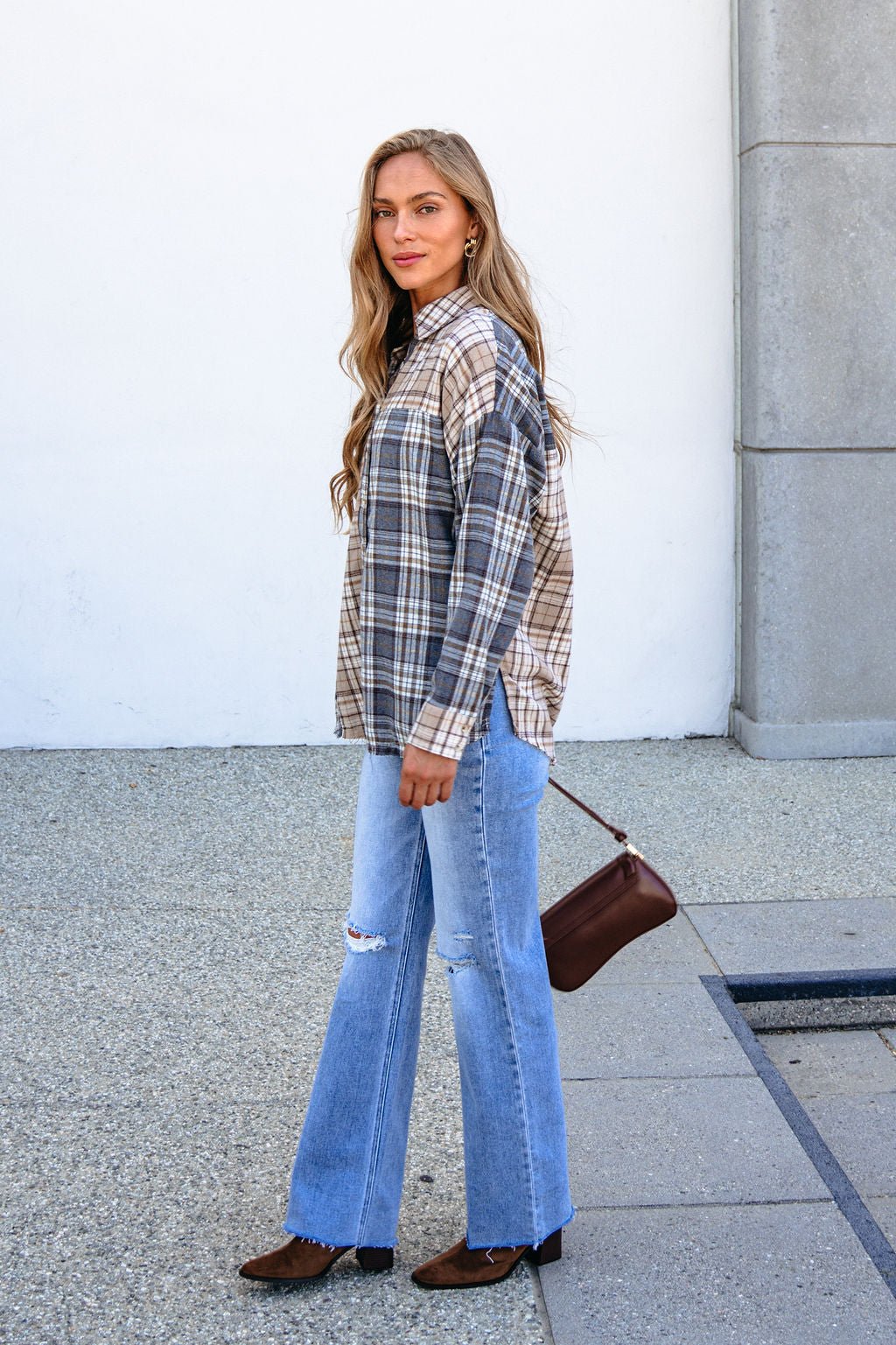 Woman in a Grey Plaid Button Down Top stands by a white wall, styled with ripped jeans and brown shoes.