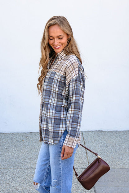 Woman in relaxed fit Grey Plaid Button Down Top and ripped jeans smiles outside, holding a brown handbag against a white wall.