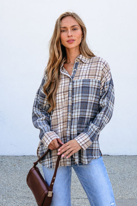 Woman wears a Grey Plaid Button Down Top and ripped jeans, holding a brown purse against a white wall.