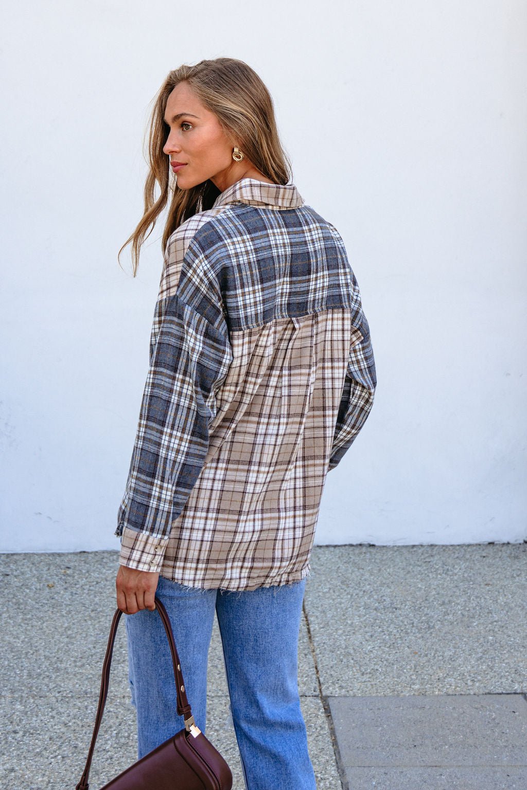 A woman wears the Grey Plaid Button Down Top outdoors, holding a brown purse and looking over her shoulder.