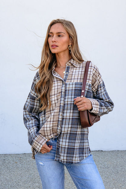 Woman with long hair wears the Grey Plaid Button Down Top and blue jeans, carrying a brown shoulder bag against a plain background.